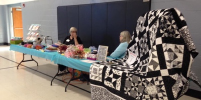 People sitting at table at event with quilts